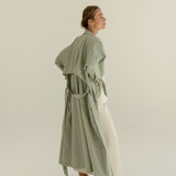 ADVA Studios Olive Green Trenchcoat from organic cotton with white merino wool skirt and black flat shoes.