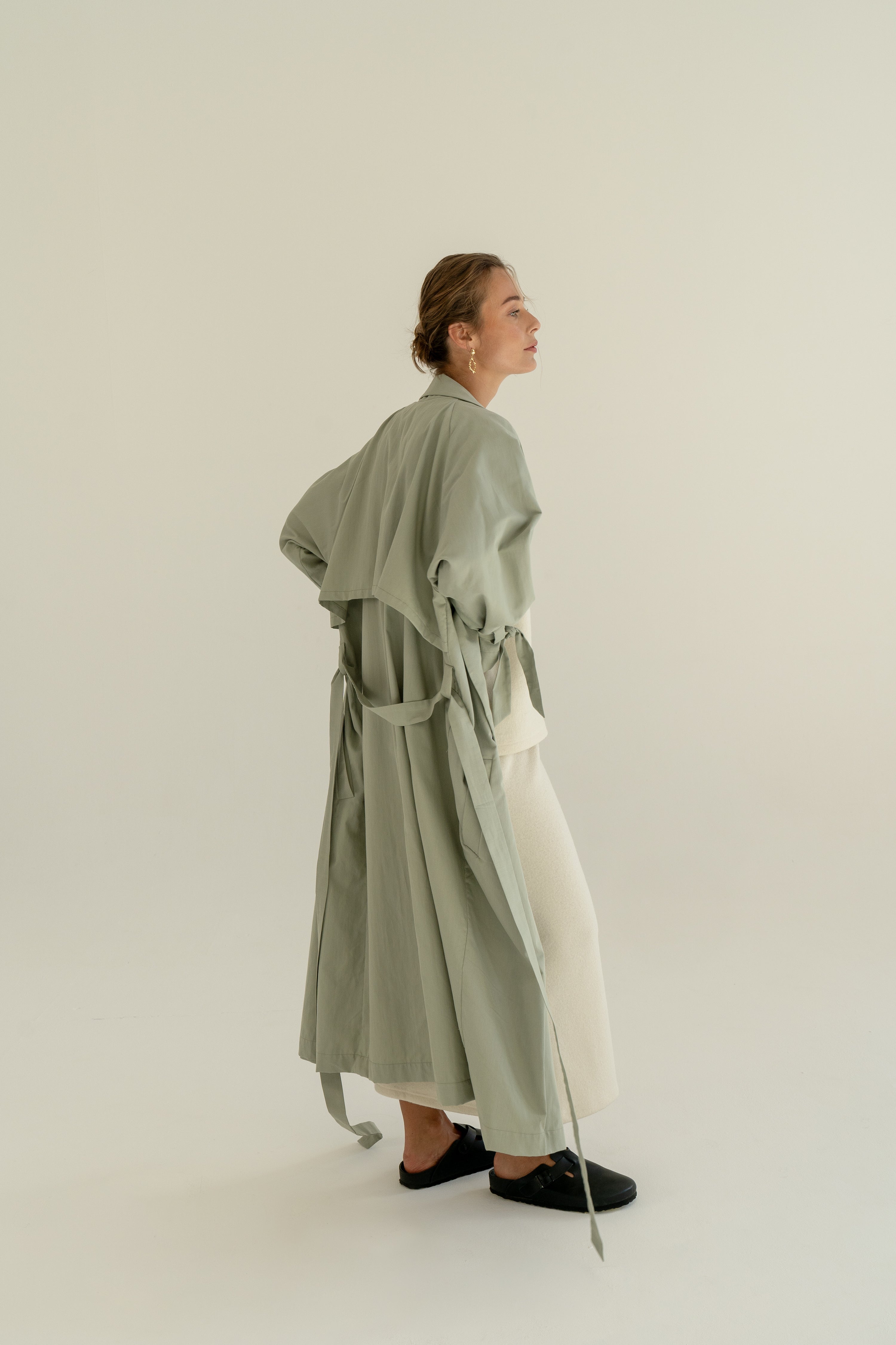 ADVA Studios Olive Green Trenchcoat from organic cotton with white merino wool skirt and black flat shoes.