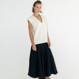 Modelka v sukni z organické bavlny v černé barvě a off-white vestě z merino vlny.