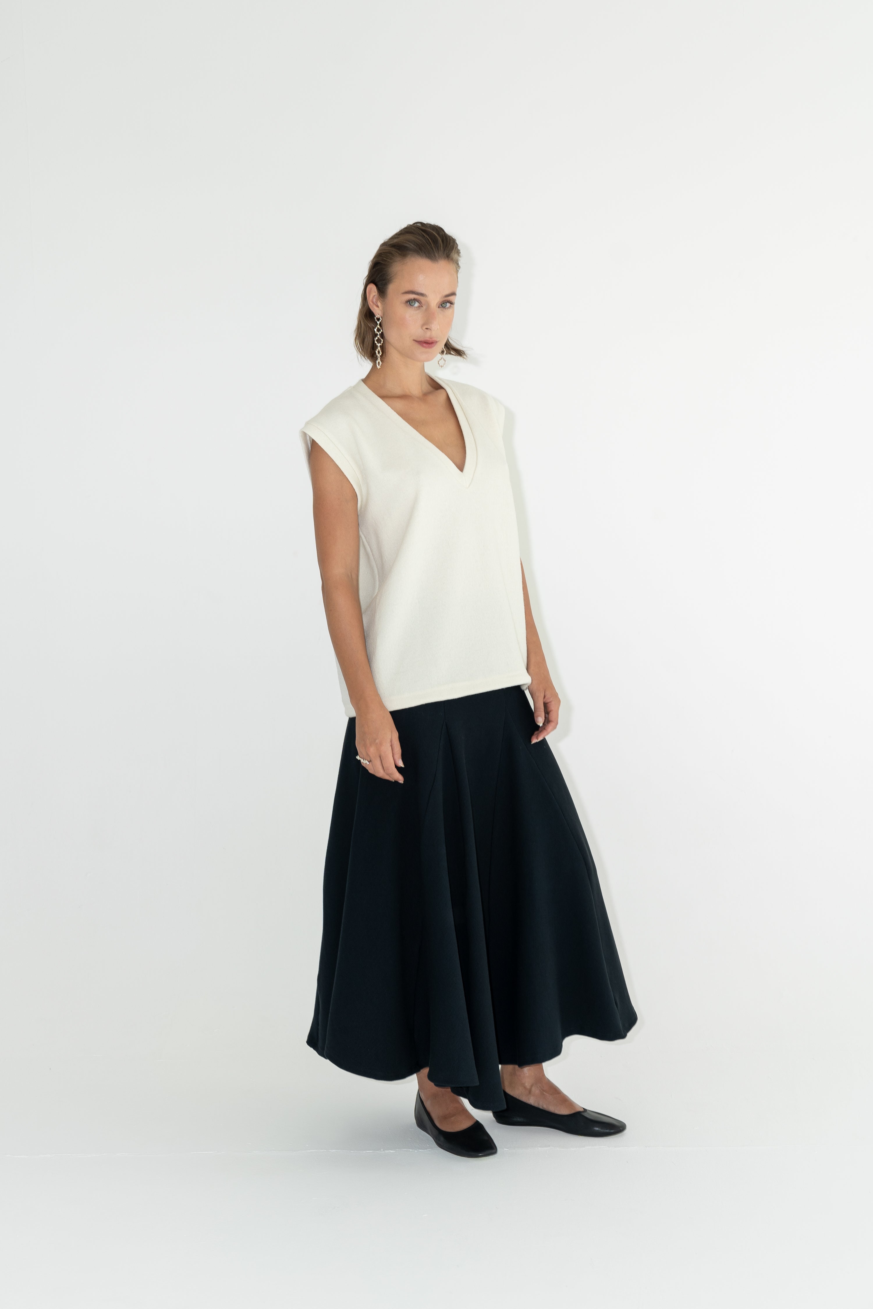 Modelka v sukni z organické bavlny v černé barvě a off-white vestě z merino vlny.