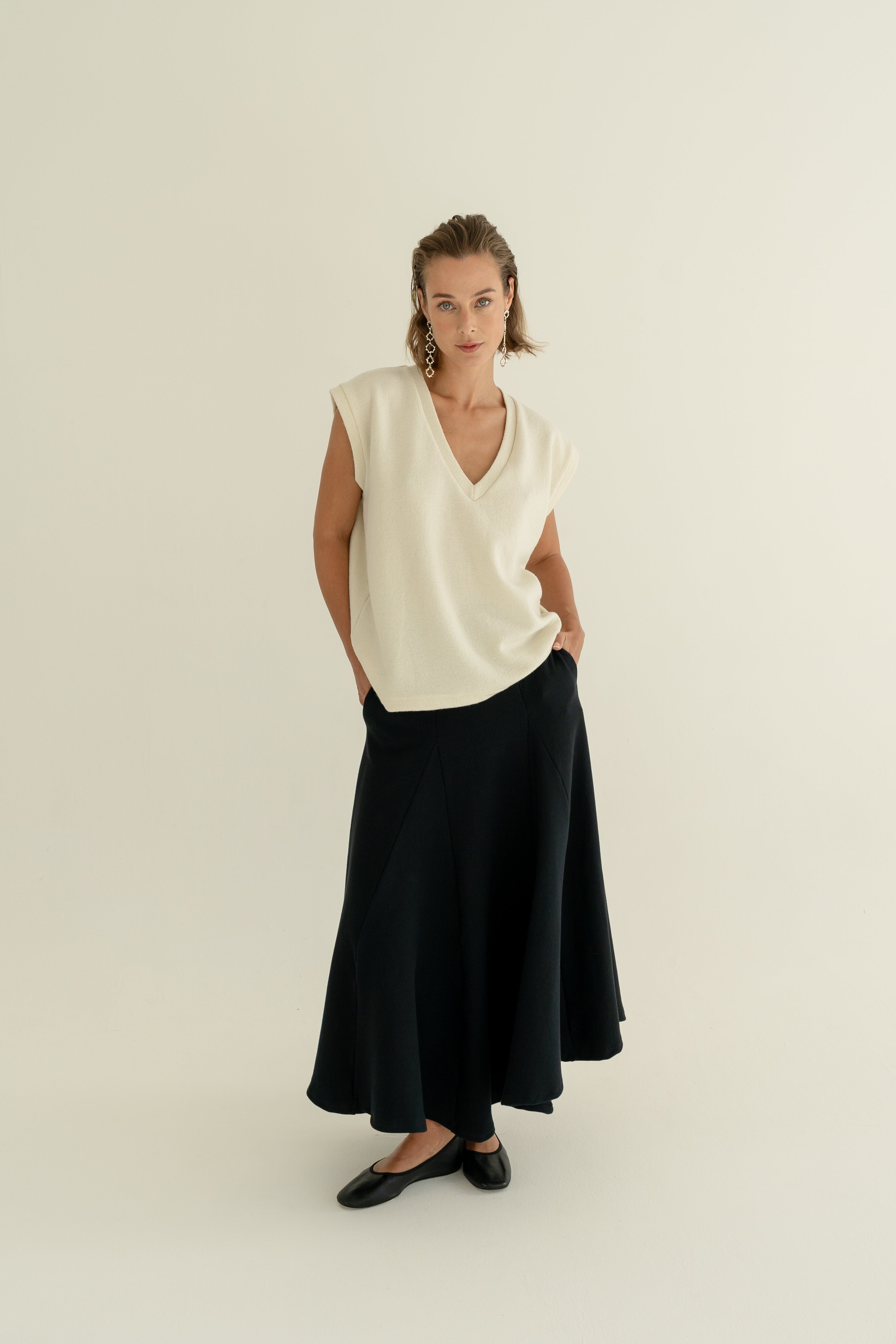 Modelka v sukni z organické bavlny v černé barvě a off-white vestě z merino vlny ADVA Studios.