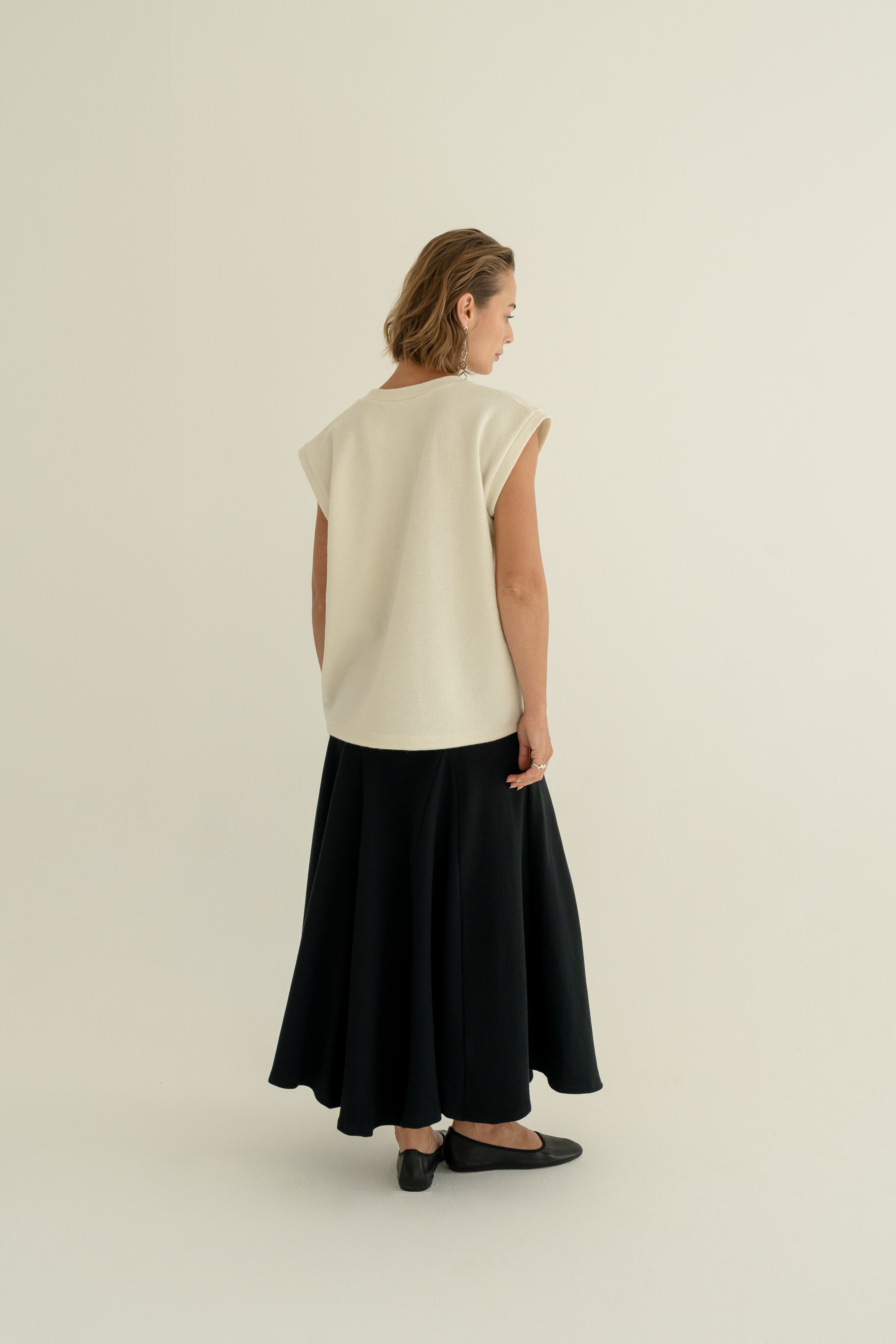 Modelka v sukni z organické bavlny v černé barvě a off-white vestě z merino vlny ADVA Studios.