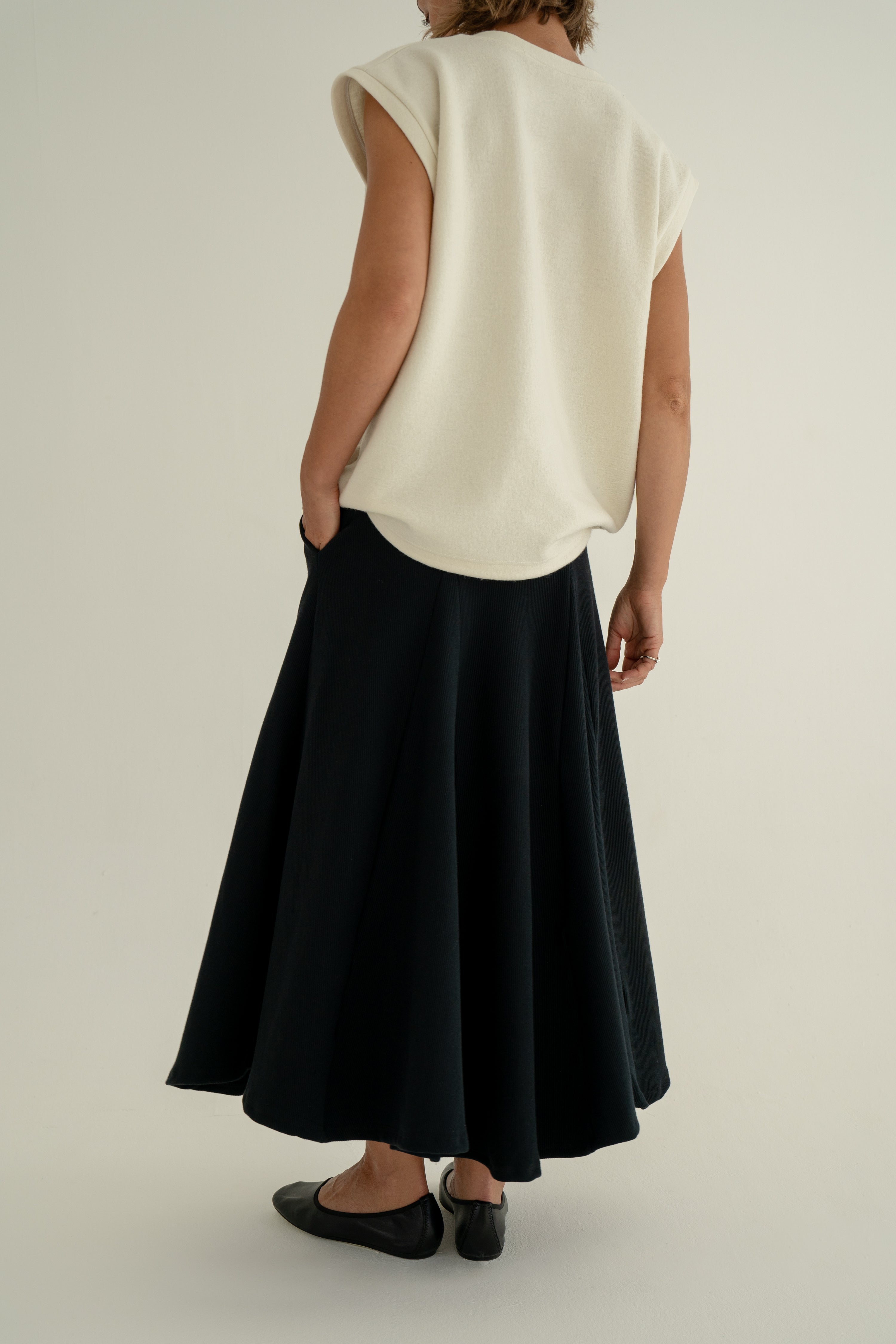 Modelka v sukni z organické bavlny v černé barvě a off-white vestě z merino vlny.
