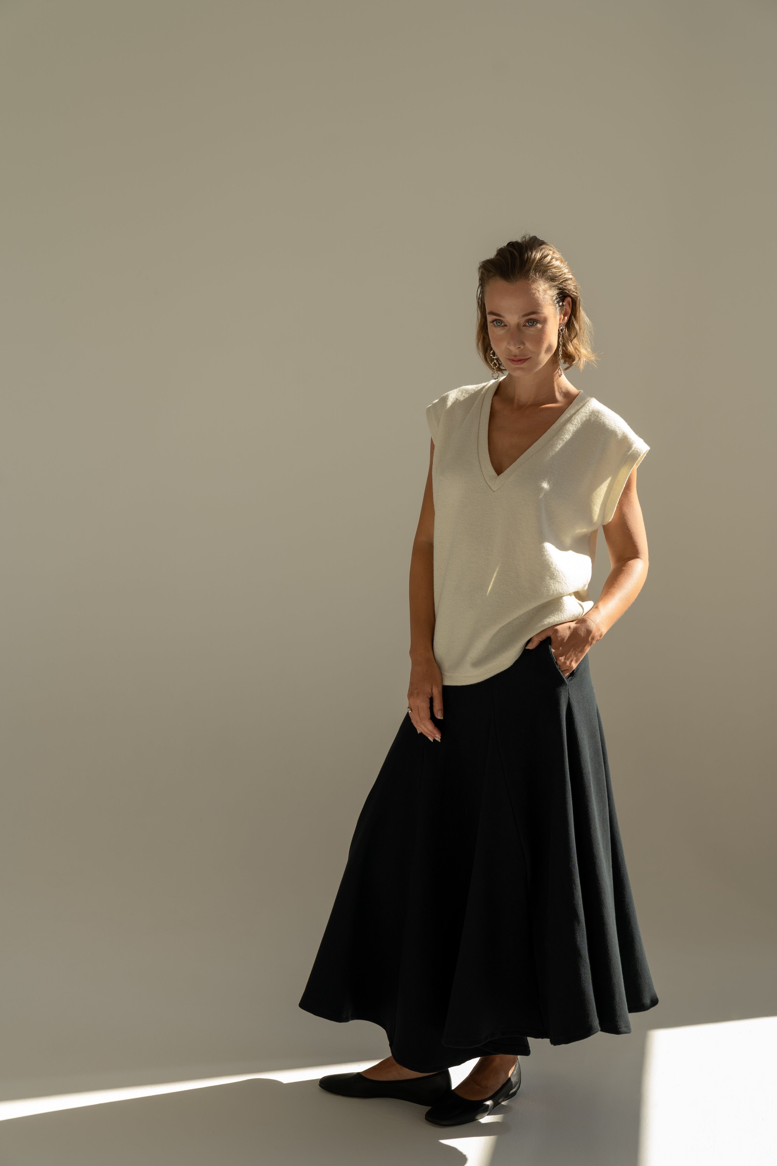 Modelka v sukni z organické bavlny v černé barvě a off-white vestě z merino vlny.