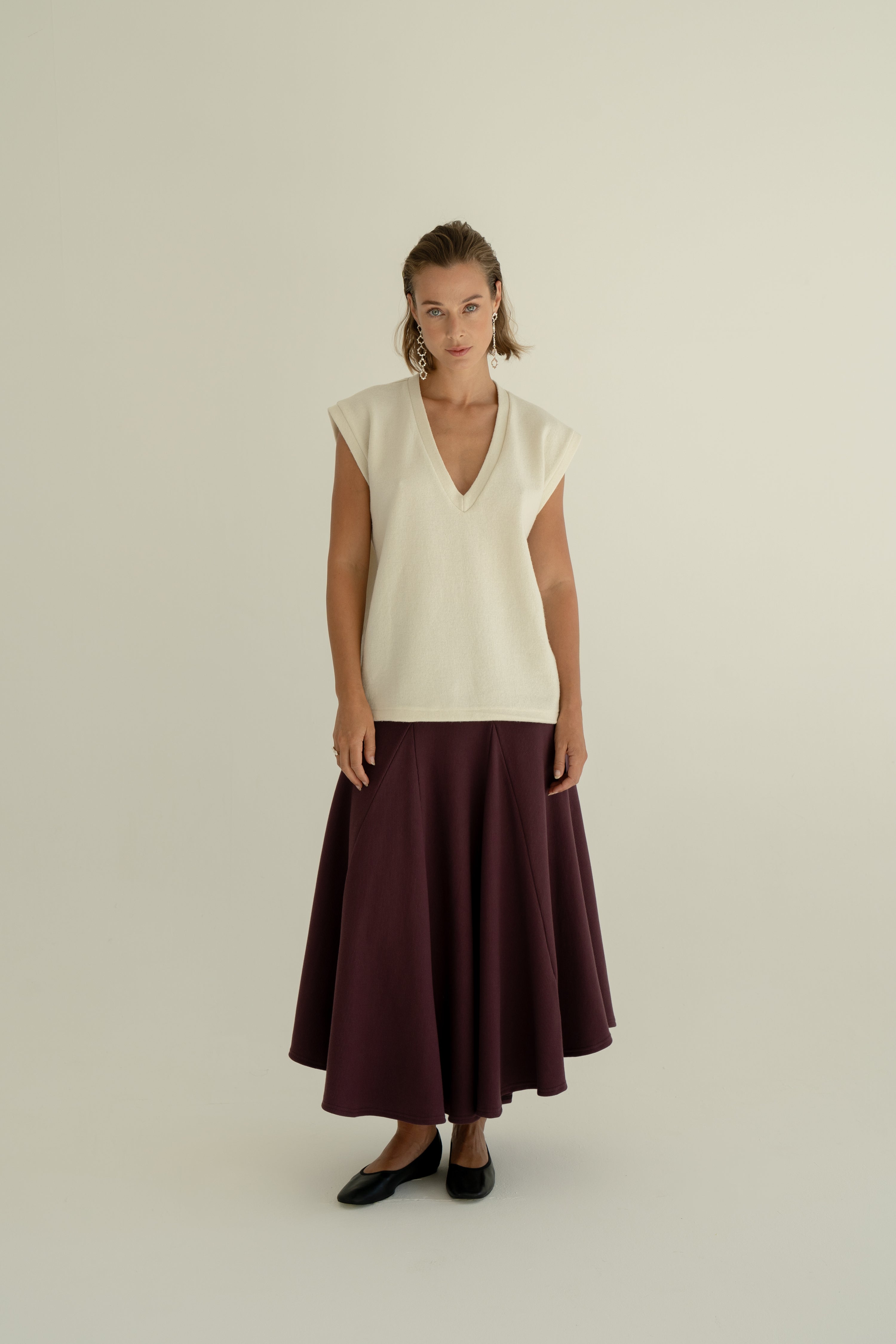 Modelka v sukni z organické bavlny ve vínové barvě a off-white vestě z merino vlny ADVA Studios.