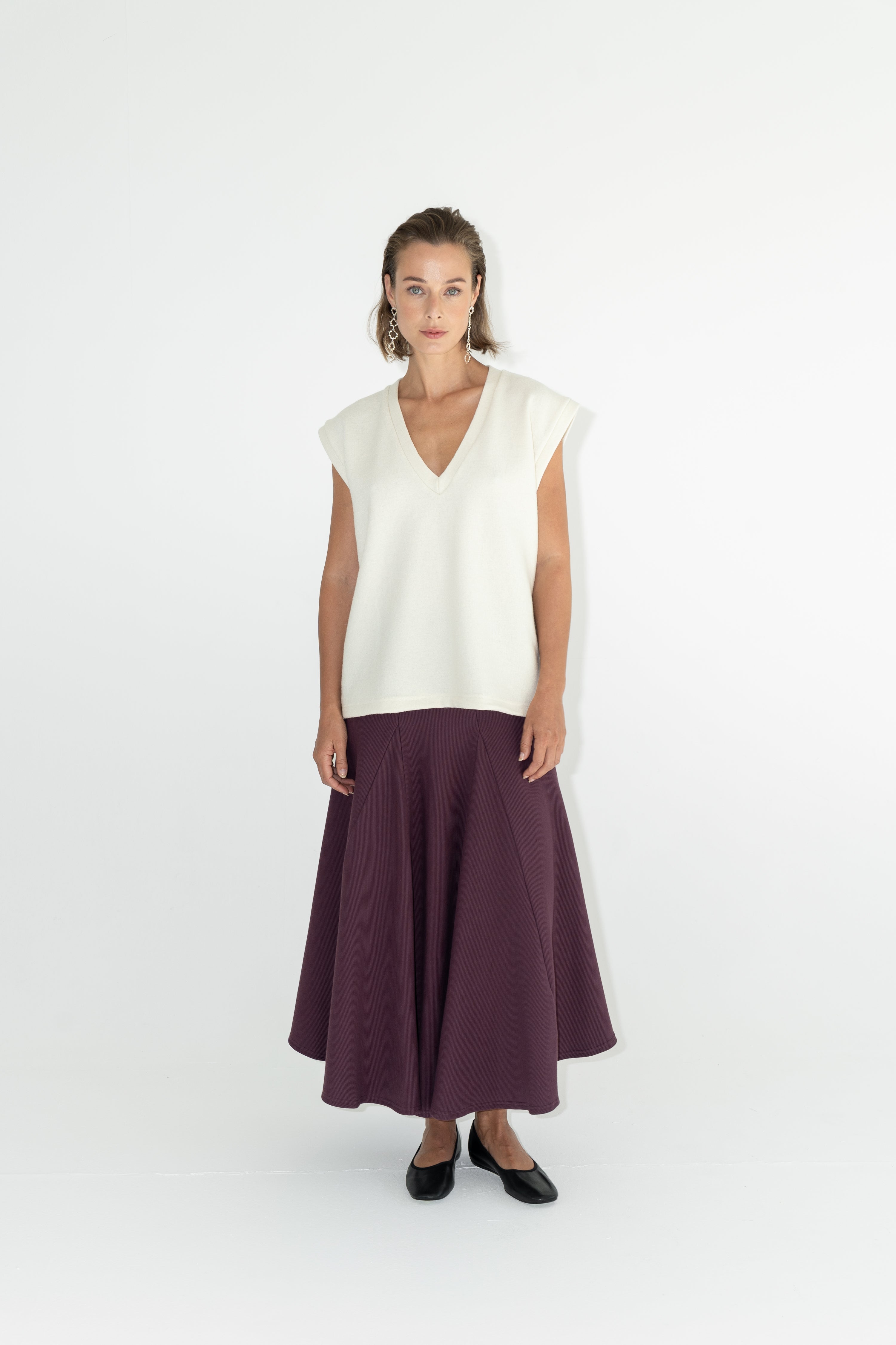 Modelka v sukni z organické bavlny ve vínové barvě a off-white vestě z merino vlny ADVA Studios.