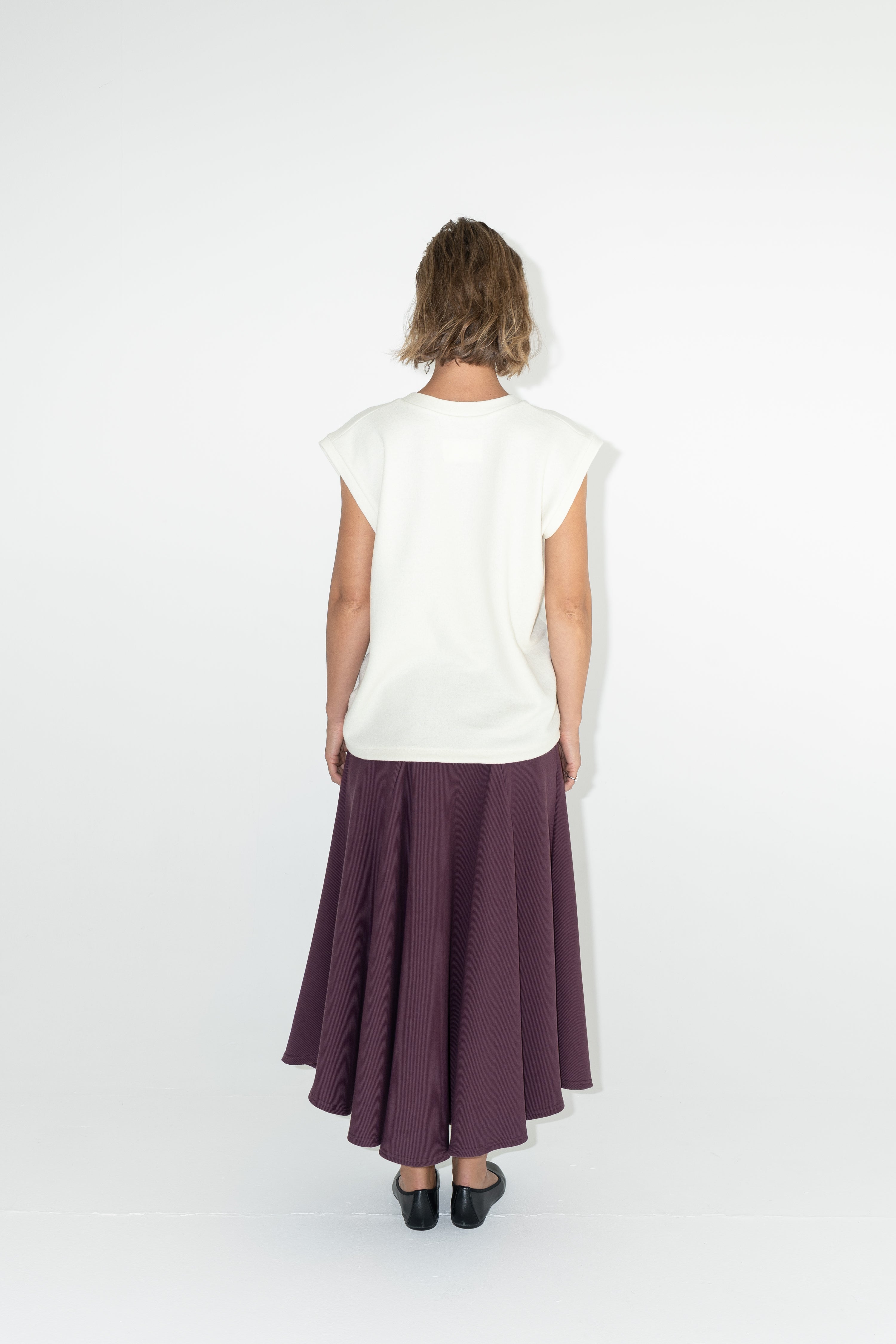 Modelka v sukni z organické bavlny ve vínové barvě a off-white vestě z merino vlny.