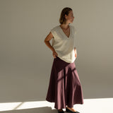 Modelka v sukni z organické bavlny ve vínové barvě a off-white vestě z merino vlny.