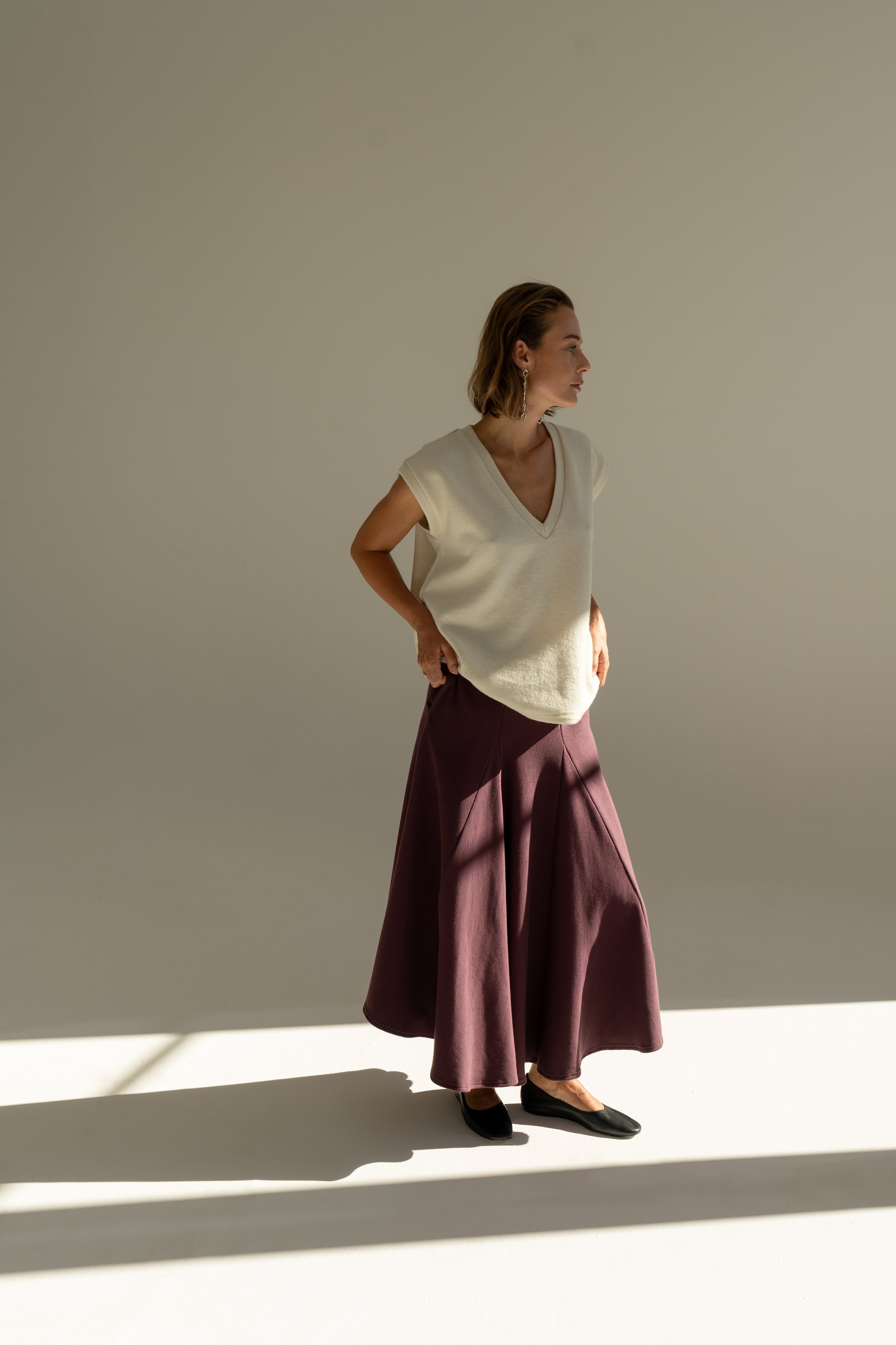 Modelka v sukni z organické bavlny ve vínové barvě a off-white vestě z merino vlny.