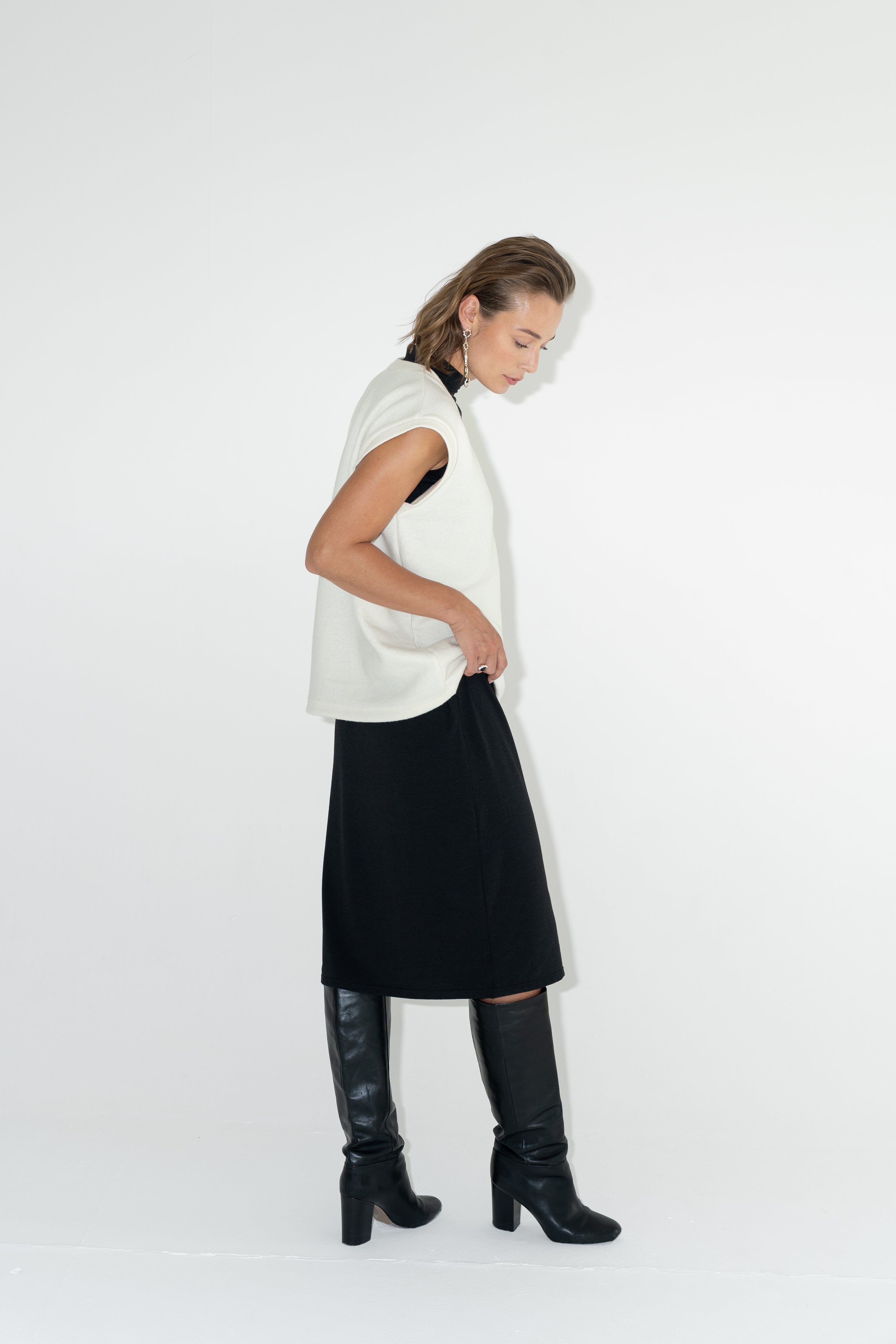 Model in black turtleneck dress with merino white vest.