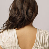 Detail zezadu stojící modelka v bílých nabíraných šatech na bílém pozadí. 