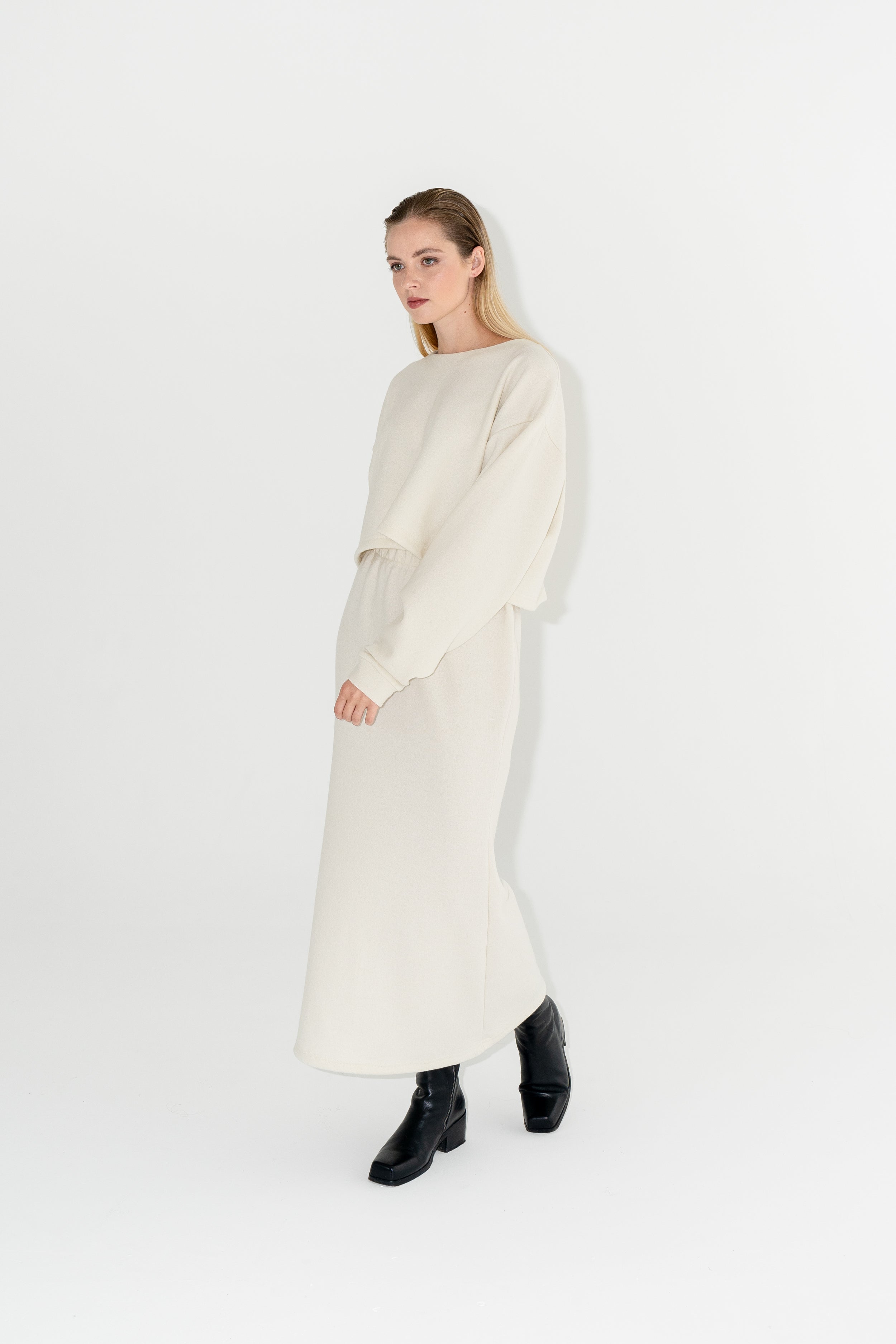 Dámský bílý set zvonkové sukně a boxy svetru s širokými rukávy z organické merino vlny s černými kozačkami.