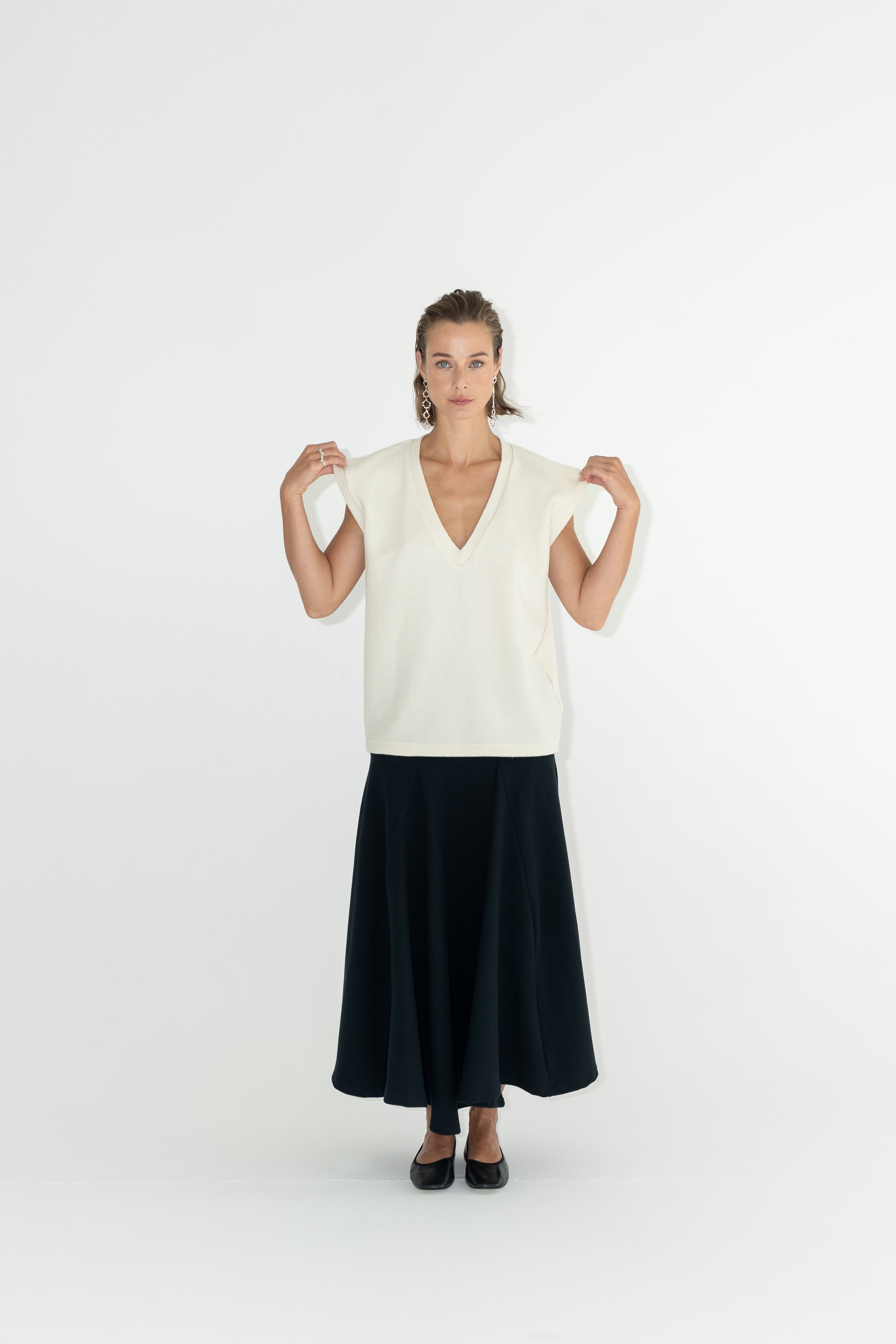 Modelka v sukni z organické bavlny v černé barvě a off-white vestě z merino vlny. 